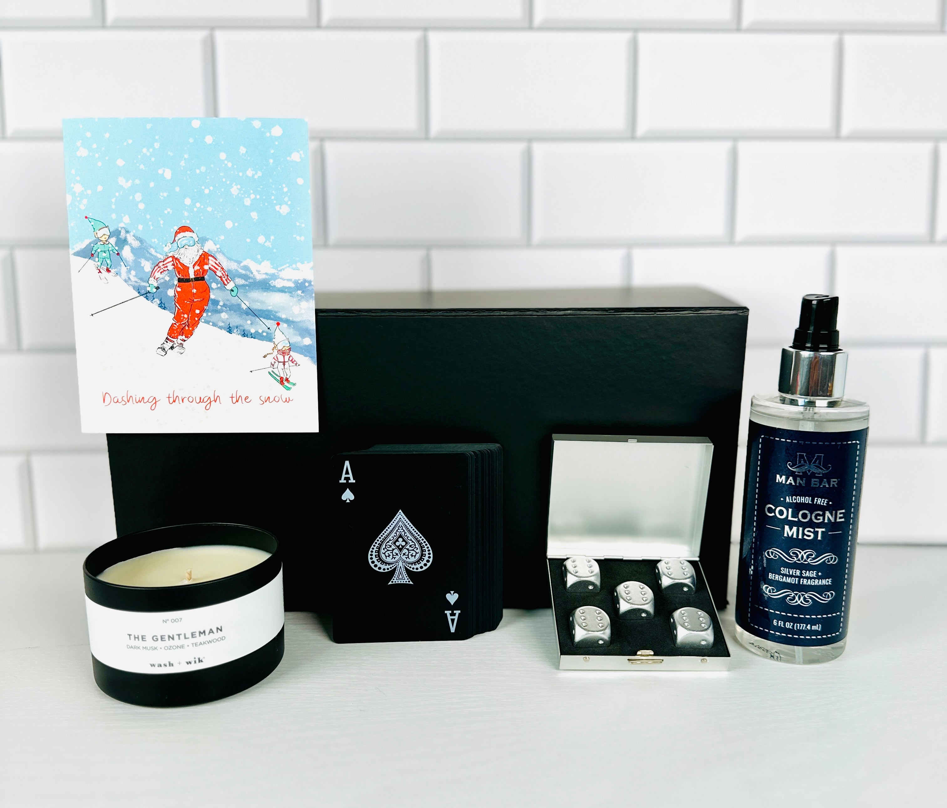A Loyal Society Men's Christmas gift set  that has a game night theme. It a winter-themed greeting card, stainless steel dice and carrying case, a relaxing masculine scented candle, a deck of waterproof playing cards and a bottle of  cologne mist.