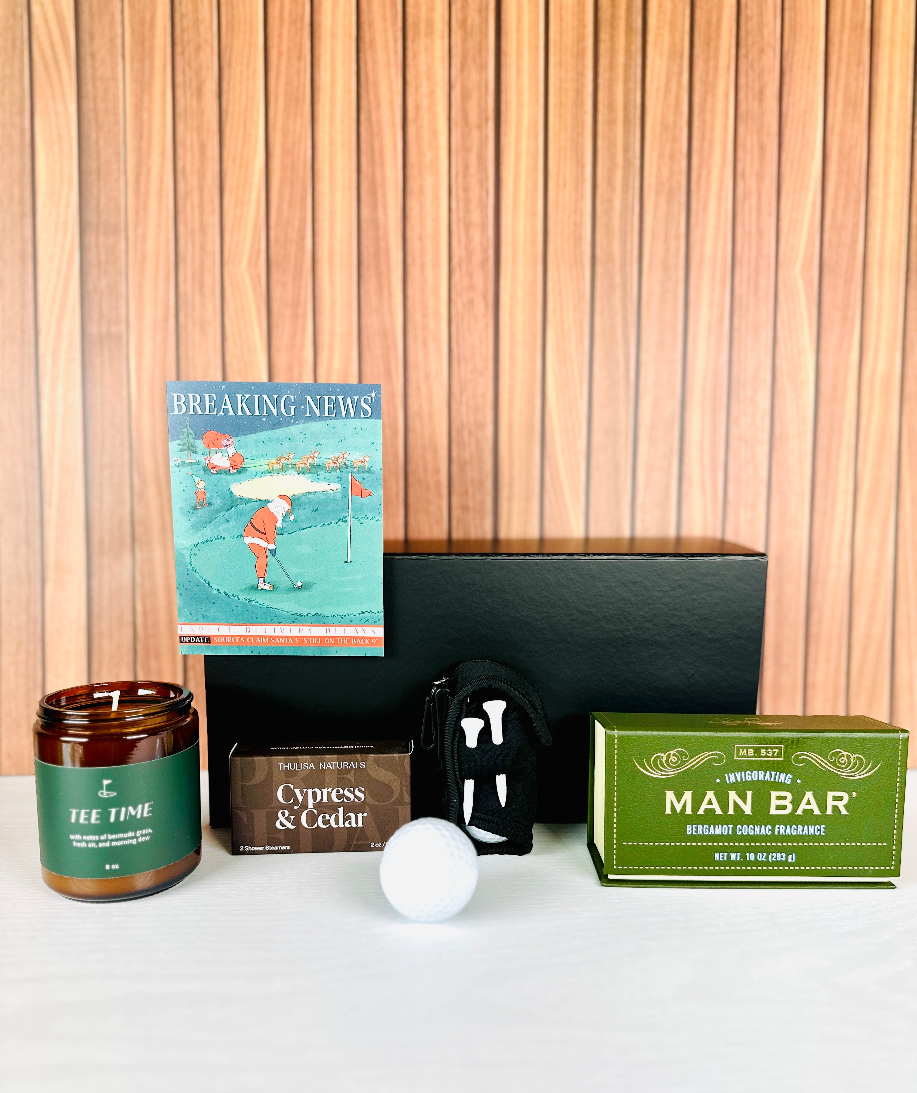 A Loyal Society Men's Christmas gift set that is a golf theme. The gift set includes 4 golf tees and 2 golf balls, along with a "tee time" scented candle. It also includes a  'Breaking News' Christmas card, a bath body bar soap and a pack of shower steamers. Great for a golf loving family member or friend!